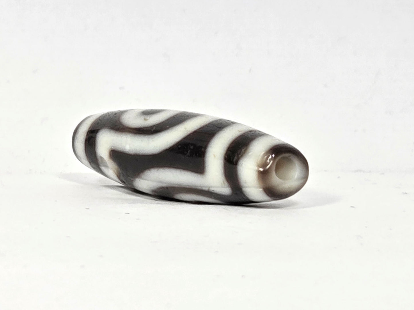 Opposite end cap of antique two eye dzi bead At-010726-2E3, dark brown agate tip with drill hole, second eye face partially visible, natural agate, unretouched