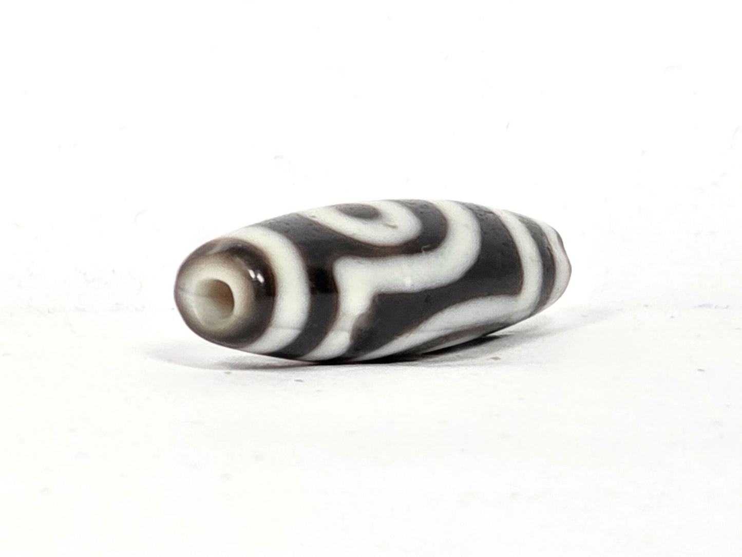 End cap view of antique two eye dzi bead At-010726-2E3, dark brown agate tip, drill hole centred, torpedo body tapering, near-black agate, 38.6mm
