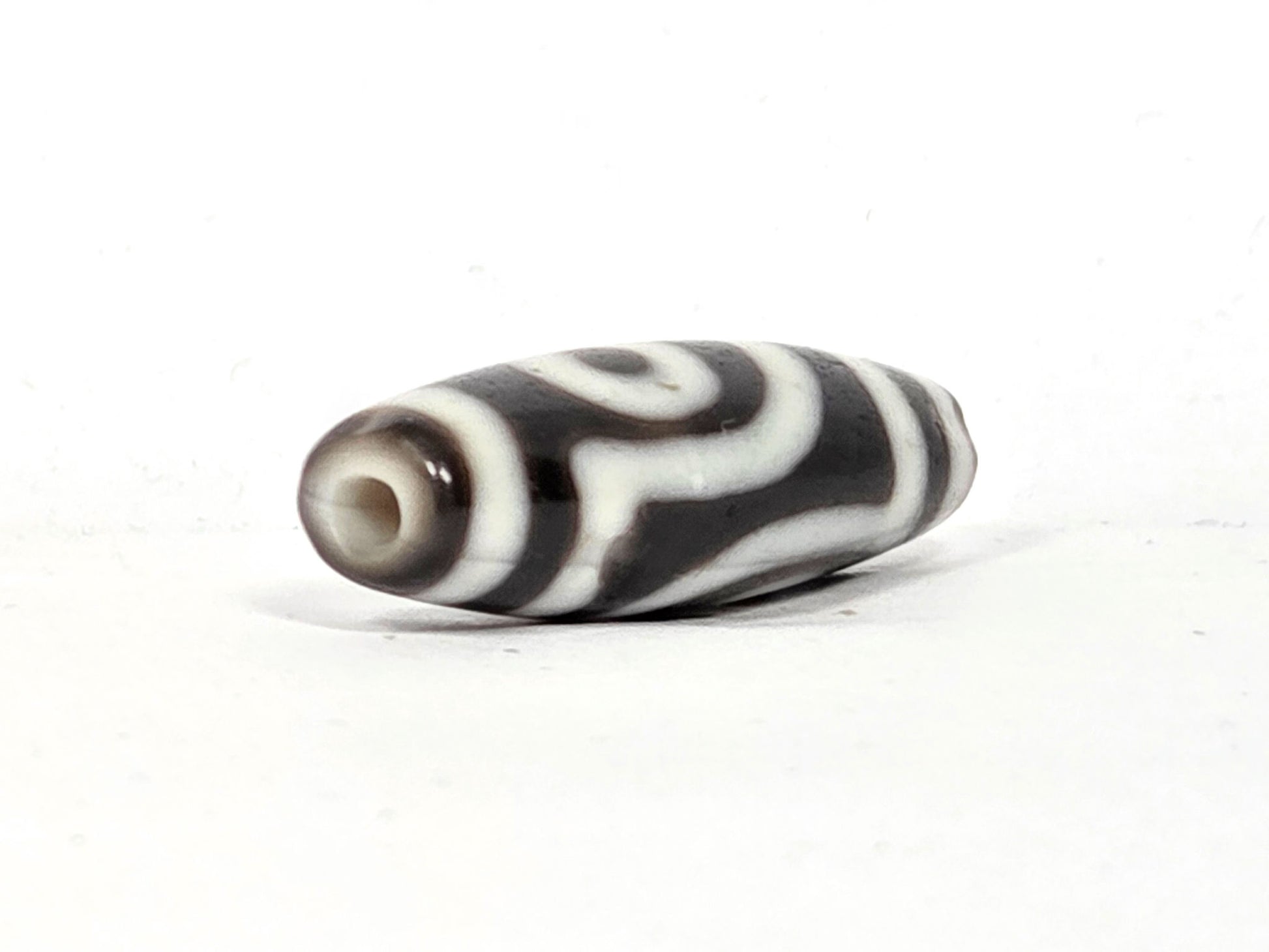 End cap view of antique two eye dzi bead At-010726-2E3, dark brown agate tip, drill hole centred, torpedo body tapering, near-black agate, 38.6mm