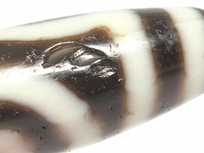 Another close detail of antique two eye dzi bead At-010726-2E3 showing medicine dig on near-black agate surface, authentic age marking, unretouched photography