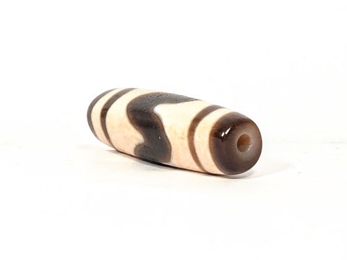 V-030326-TTBS vintage tiger tooth dzi, angled end shot, cream end cap, drill hole visible, dark motif zone, unretouched.