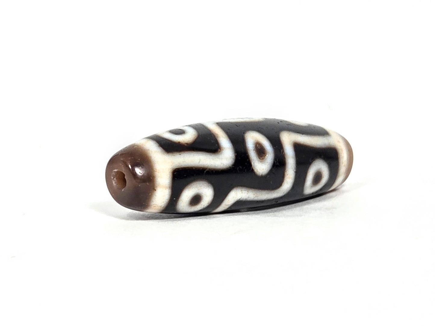At-070626-9EBS nine eye dzi, angled drill end B, warm brown domed end cap, drill hole visible, cream eye motif, unretouched