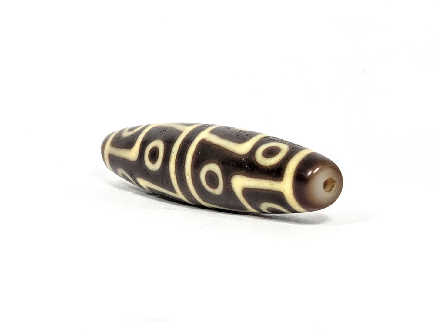 Ac-070826-12E ancient twelve eye dzi bead angled view showing warm reddish-brown drill end cap profile unretouched
