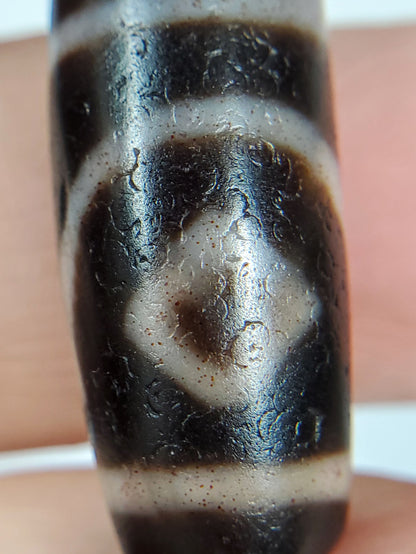 Macro: ancient dzi diamond eye — brown-black bloodspot at centre, heavy micro-crystalline crackle pitting, Anc-0426-2DE