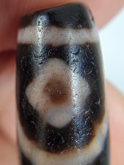 Macro: ancient dzi first diamond eye — brown bloodspot pooling at centre, crackle surface pitting, Anc-0426-2DE