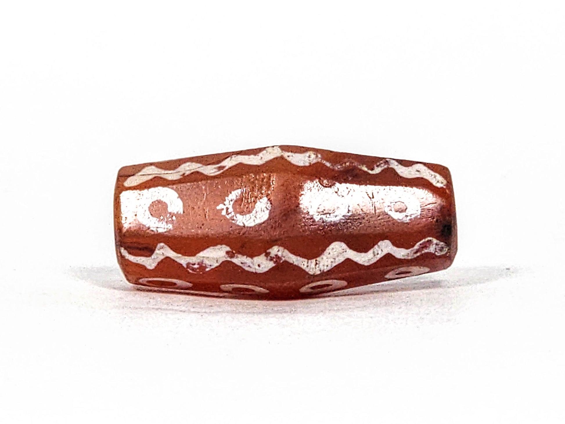 Ac-010825-16EW hero angled, 24.1×11.0mm terracotta-red carnelian, eye rings and wave bands visible, octagonal, unretouched