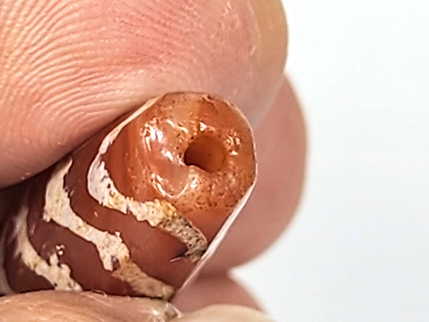 Ac-030525-5TS macro End B, funnel-shaped ancient drill hole, worn rim, warm terracotta carnelian, unretouched