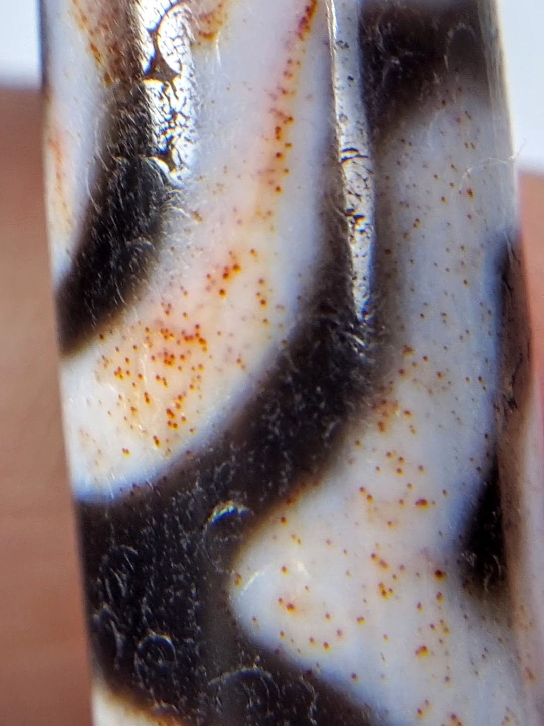 Close-up of Three Eye motif etching on antique Tibetan Dzi bead — bold white line with cinnabar orange-rust bloodspot staining in surrounding natural agate