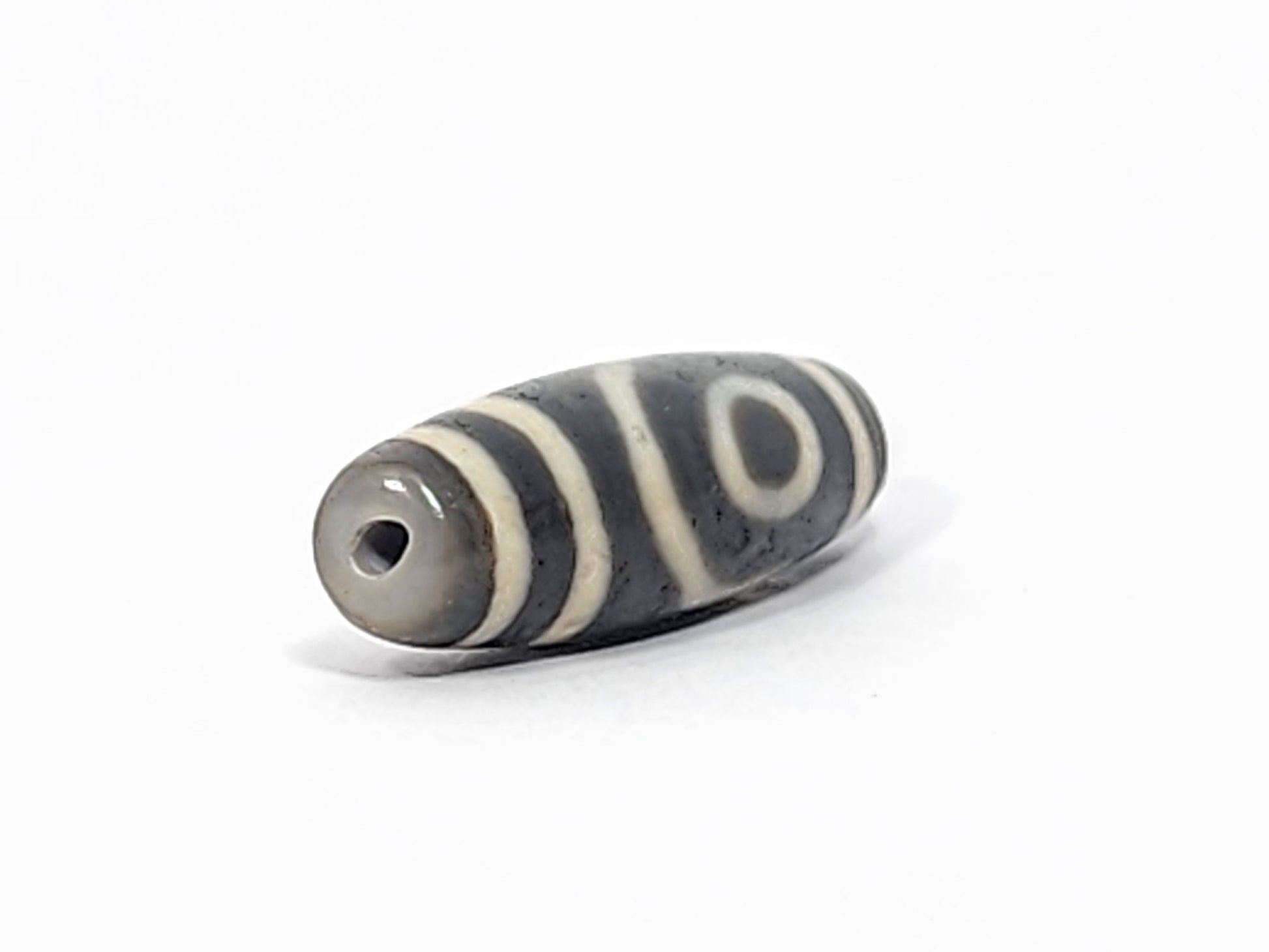 Ac-052525-2E left drill hole end, cool grey-brown tip, concentric ring eye visible from end angle, unretouched