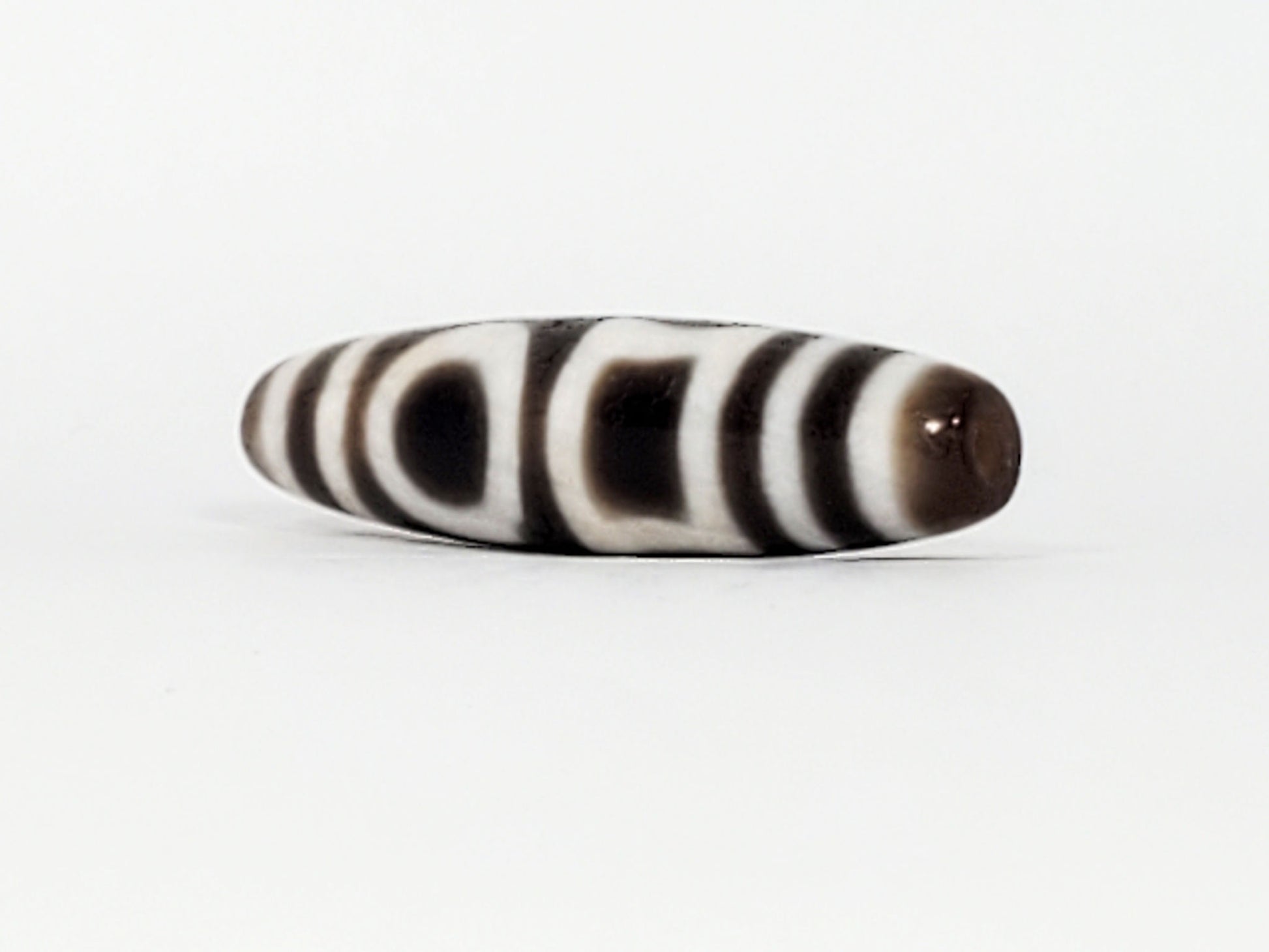 Angled end of antique Double H&E Dzi — drill hole, stripe bands wrapping to tip, tapered profile