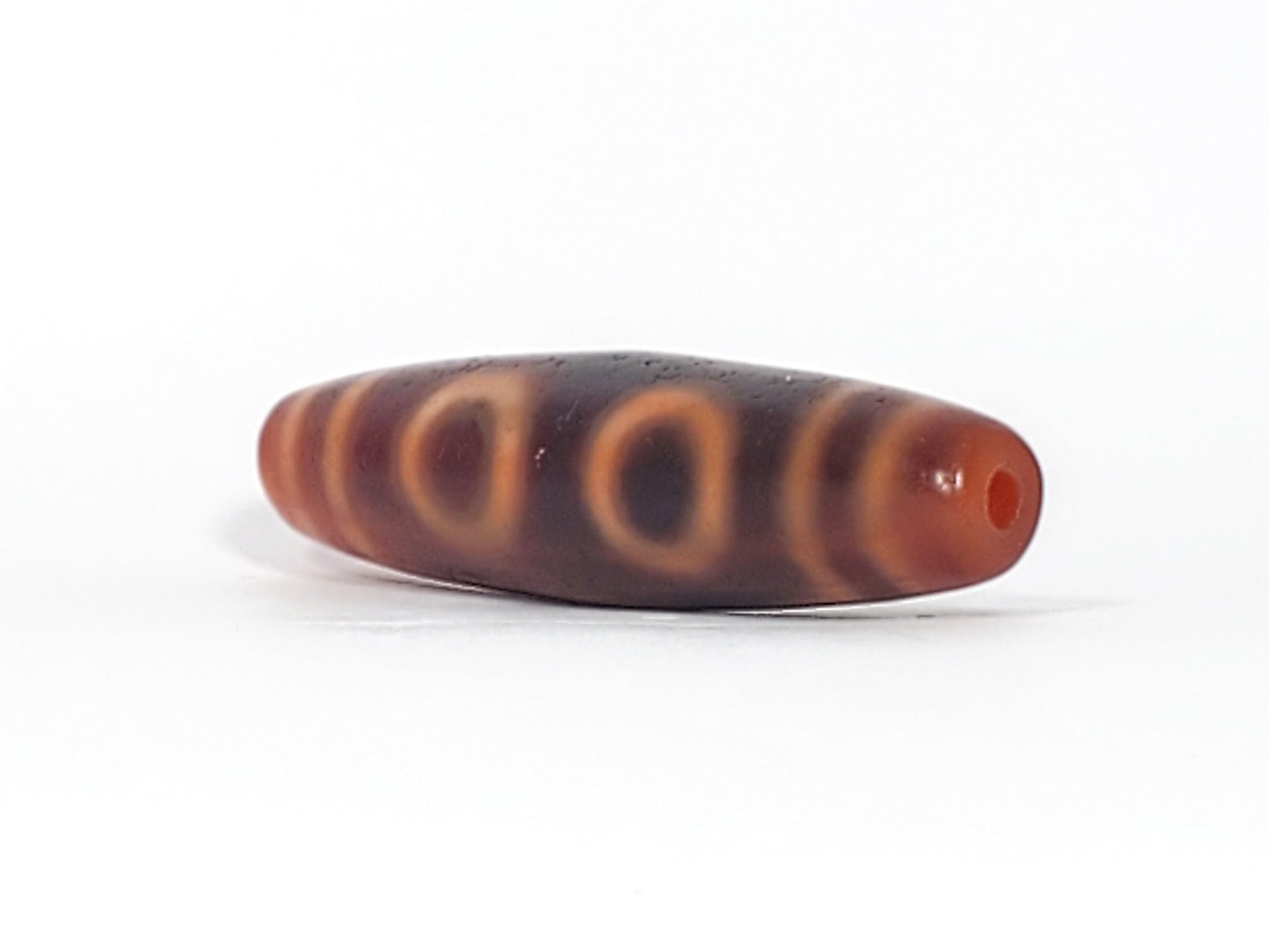 At-060126-4E2, angled End B, terracotta-orange end cap and drilled hole, two C-ring eyes visible on dark body, unretouched