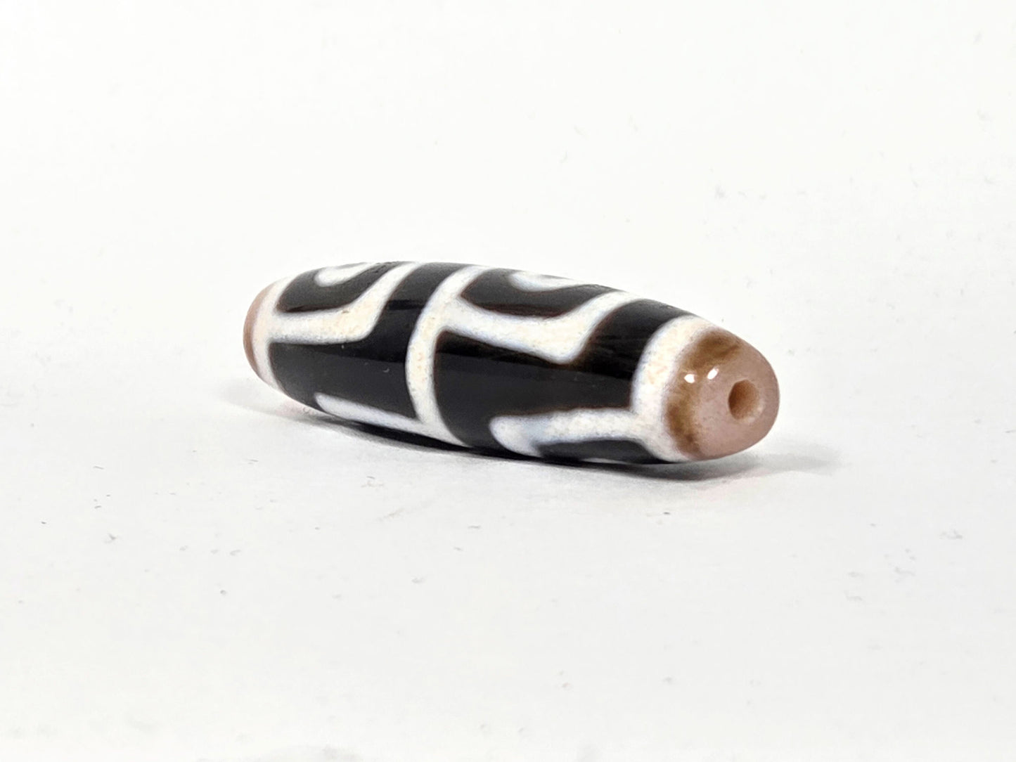 At-042626-4E3 End A, warm sandy-tan end cap, centred drill hole, pitch-black body, white lines, unretouched