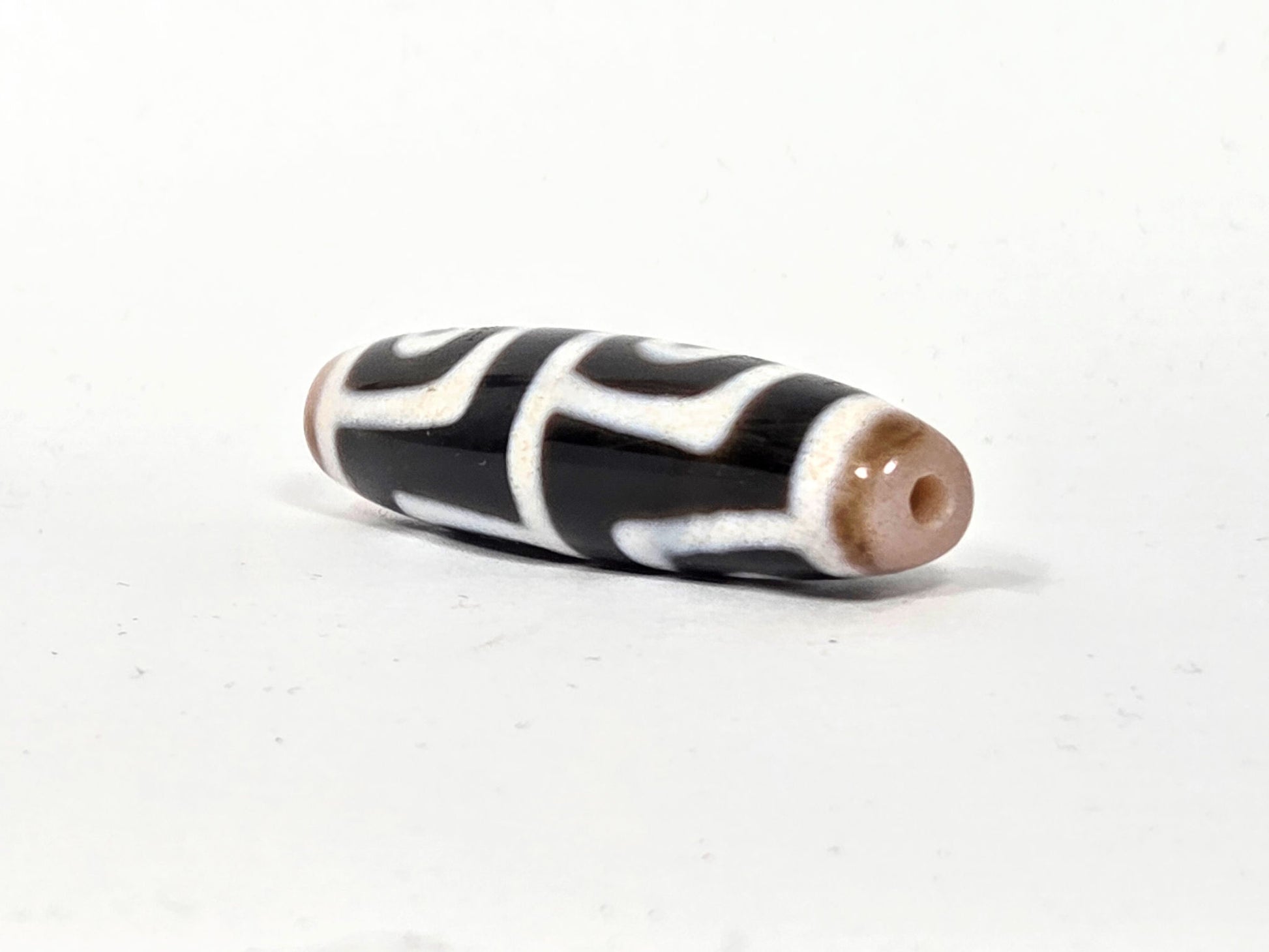 At-042626-4E3 End A, warm sandy-tan end cap, centred drill hole, pitch-black body, white lines, unretouched
