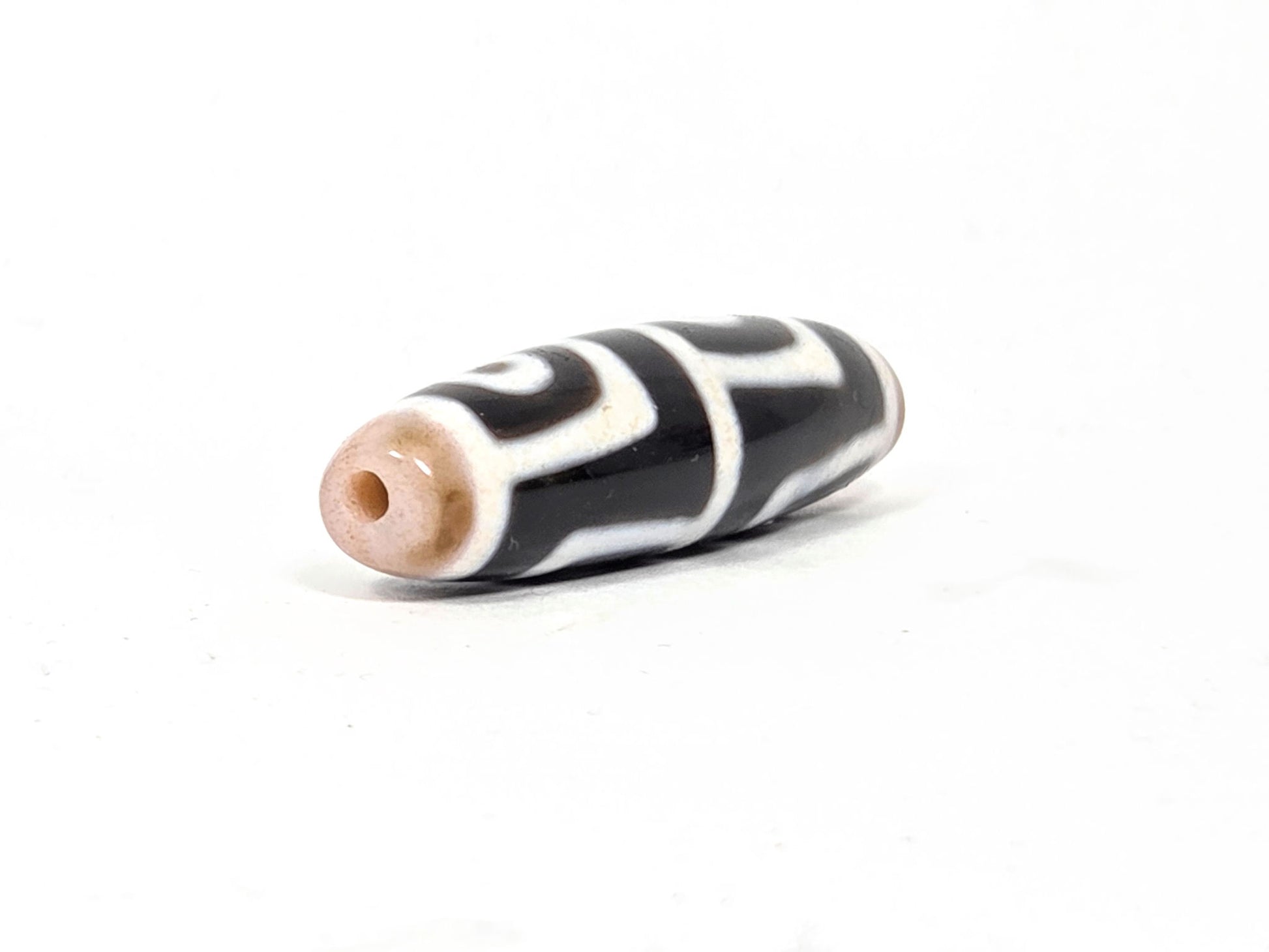 At-042626-4E3 End B, warm sandy-tan end cap, clean drill hole, pitch-black body with white motif, unretouched