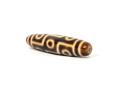 Angled end view of antique Nine Eye dzi bead showing dark warm brown end cap with drill hole and eye network, At-083025-9E3