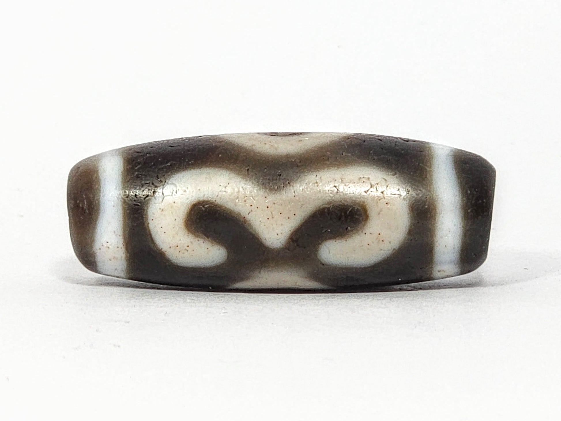 Face C of antique Double Bat Two Eye dzi At-060725-DB2E2, bat motif reversed showing calligraphic scrollwork wing-tips, cream-dominant field on grey-brown agate, unretouched