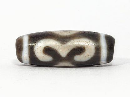 Face C of antique Double Bat Two Eye dzi At-060725-DB2E2, bat motif reversed showing calligraphic scrollwork wing-tips, cream-dominant field on grey-brown agate, unretouched