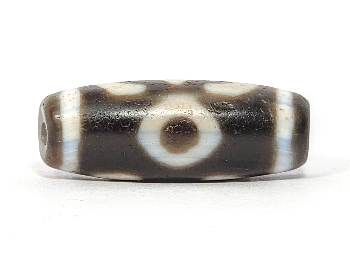 Face D of antique Double Bat Two Eye dzi At-060725-DB2E2, second concentric-ring eye on grey-brown agate, drill hole visible at end cap edge, cream surround field, unretouched