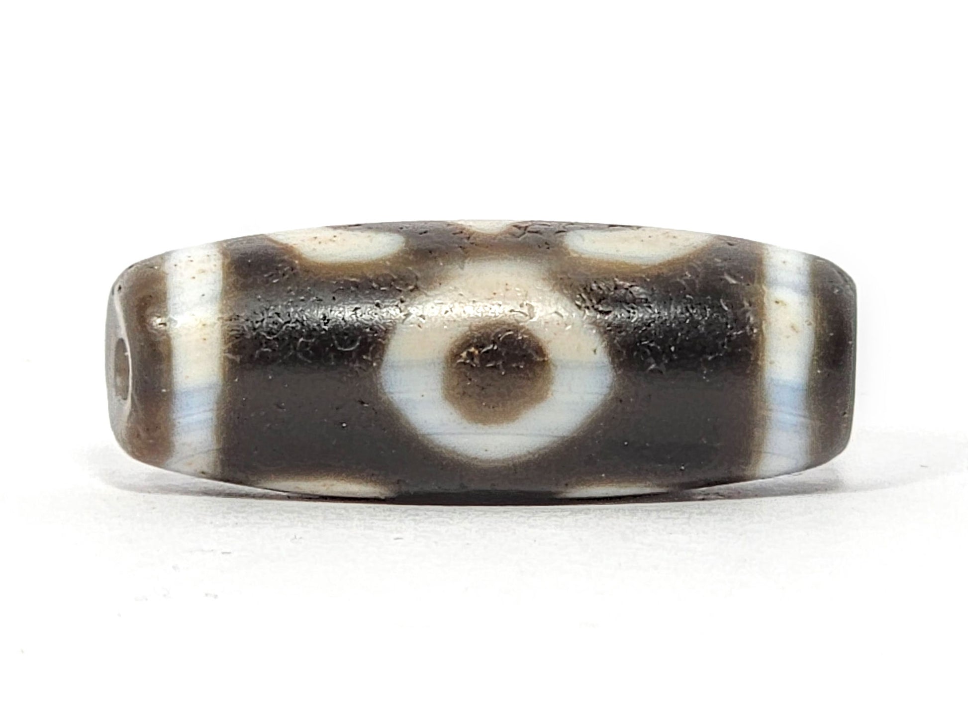 Face D of antique Double Bat Two Eye dzi At-060725-DB2E2, second concentric-ring eye on grey-brown agate, drill hole visible at end cap edge, cream surround field, unretouched