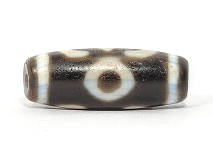 Face D of antique Double Bat Two Eye dzi At-060725-DB2E2, second concentric-ring eye on grey-brown agate, drill hole visible at end cap edge, cream surround field, unretouched