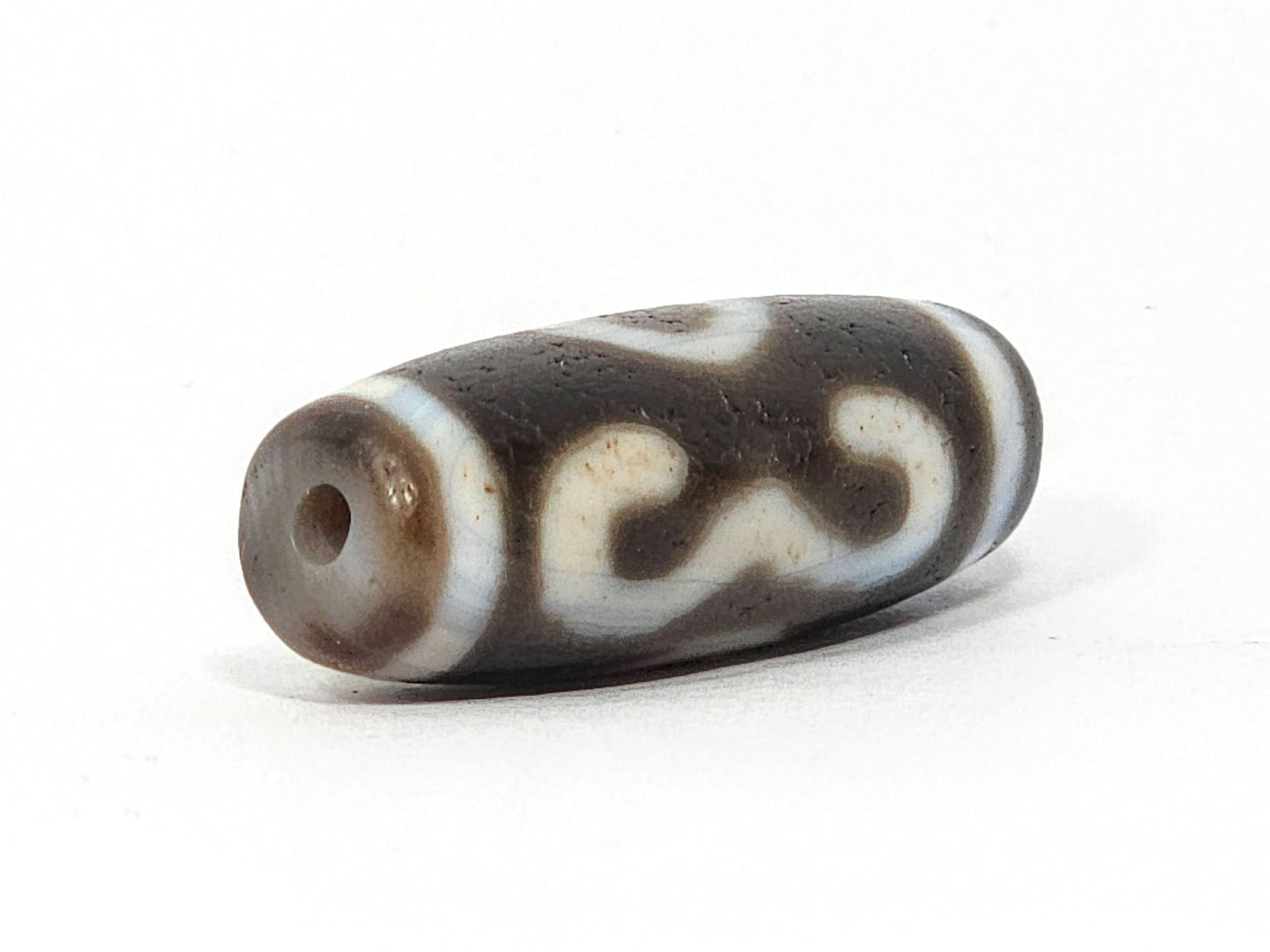 Opposite end of antique Double Bat Two Eye dzi At-060725-DB2E2, grey-brown end cap, drill hole, bat S-curve motif wrapping rectangular barrel, aged agate surface texture, unretouched