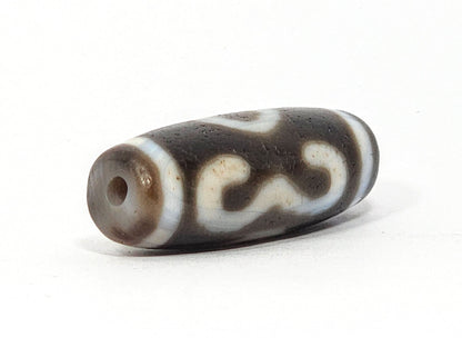 Opposite end of antique Double Bat Two Eye dzi At-060725-DB2E2, grey-brown end cap, drill hole, bat S-curve motif wrapping rectangular barrel, aged agate surface texture, unretouched