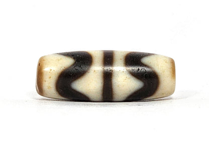 Second face of antique Double Wave dzi At-072325-DW5, cream double wave motif on warm brown agate, compact barrel form, flanking vertical stripes visible, 28.4mm, unretouched