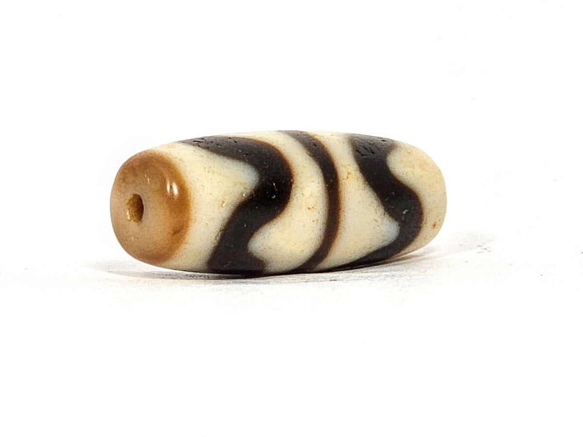 Opposite angle of antique Double Wave dzi At-072325-DW5, warm brown agate, cream wave S-curves, natural weathering marks on surface, compact torpedo profile, unretouched