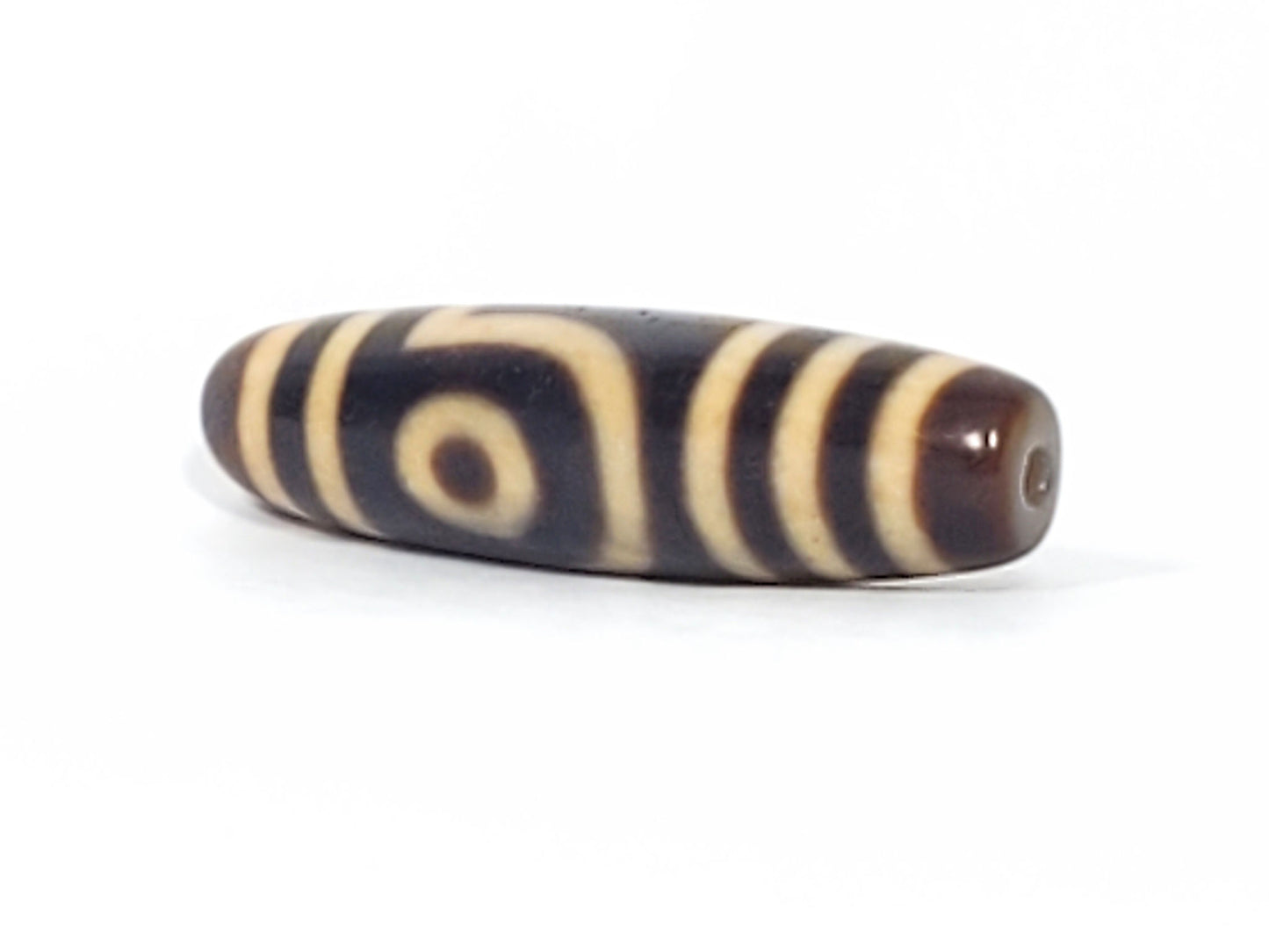 Three-quarter view of antique two eye dzi bead At-052526-2E2 showing brown drilled end cap and eye face, torpedo body profile, near-black agate, unretouched photography