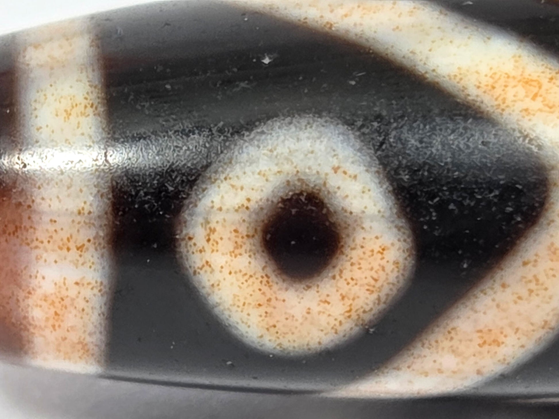 Extreme macro of eye circle on antique Eight Eye Dzi — amber cinnabar bloodspot dust in cream etching zone