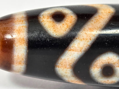 Macro of eye circles and tiger tooth on antique Dzi — vivid orange cinnabar saturation throughout etching
