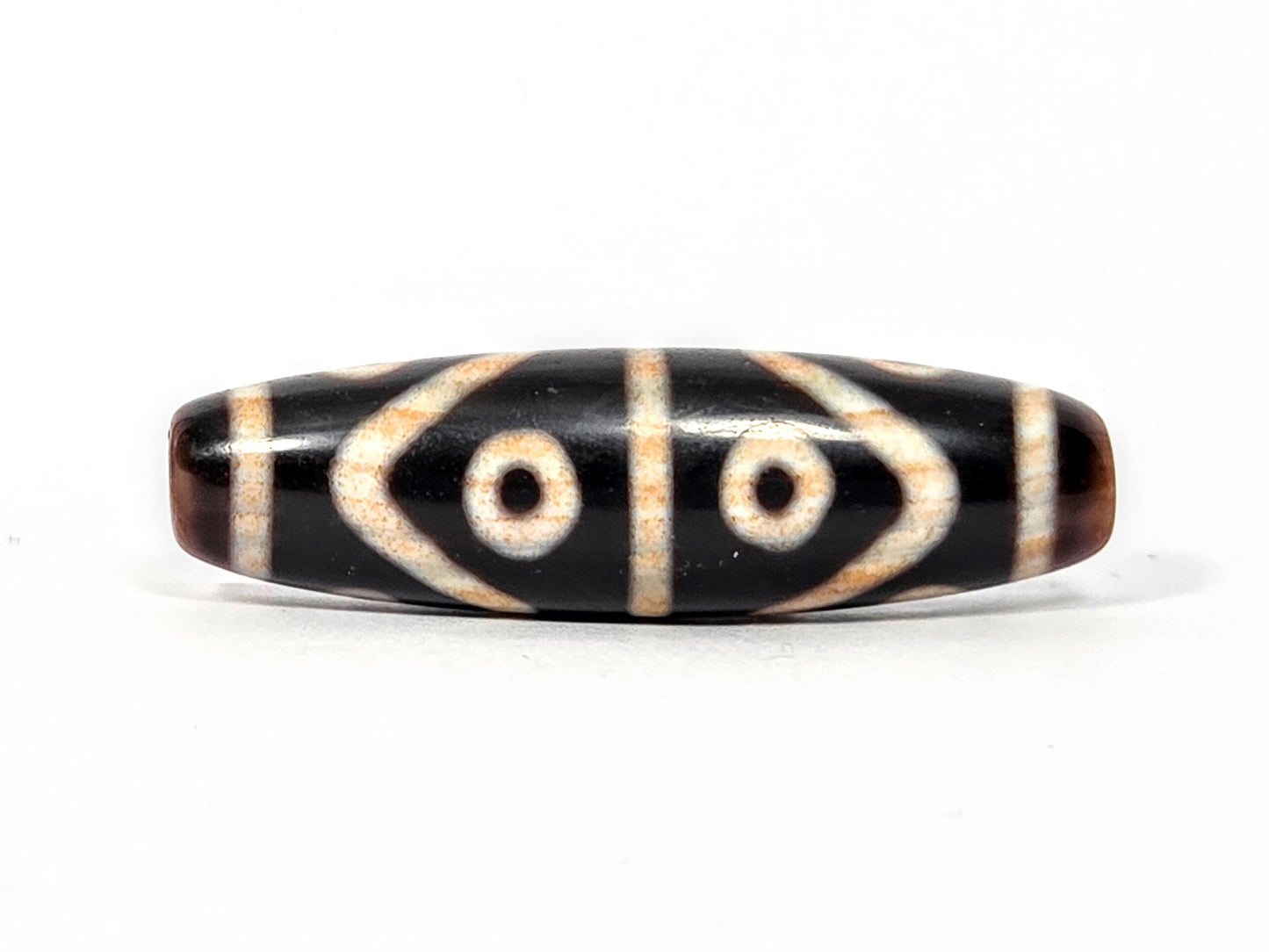Fourth face of antique Eight Eye Tiger Tooth Dzi — eye circles, tiger tooth forms, warm brown ends