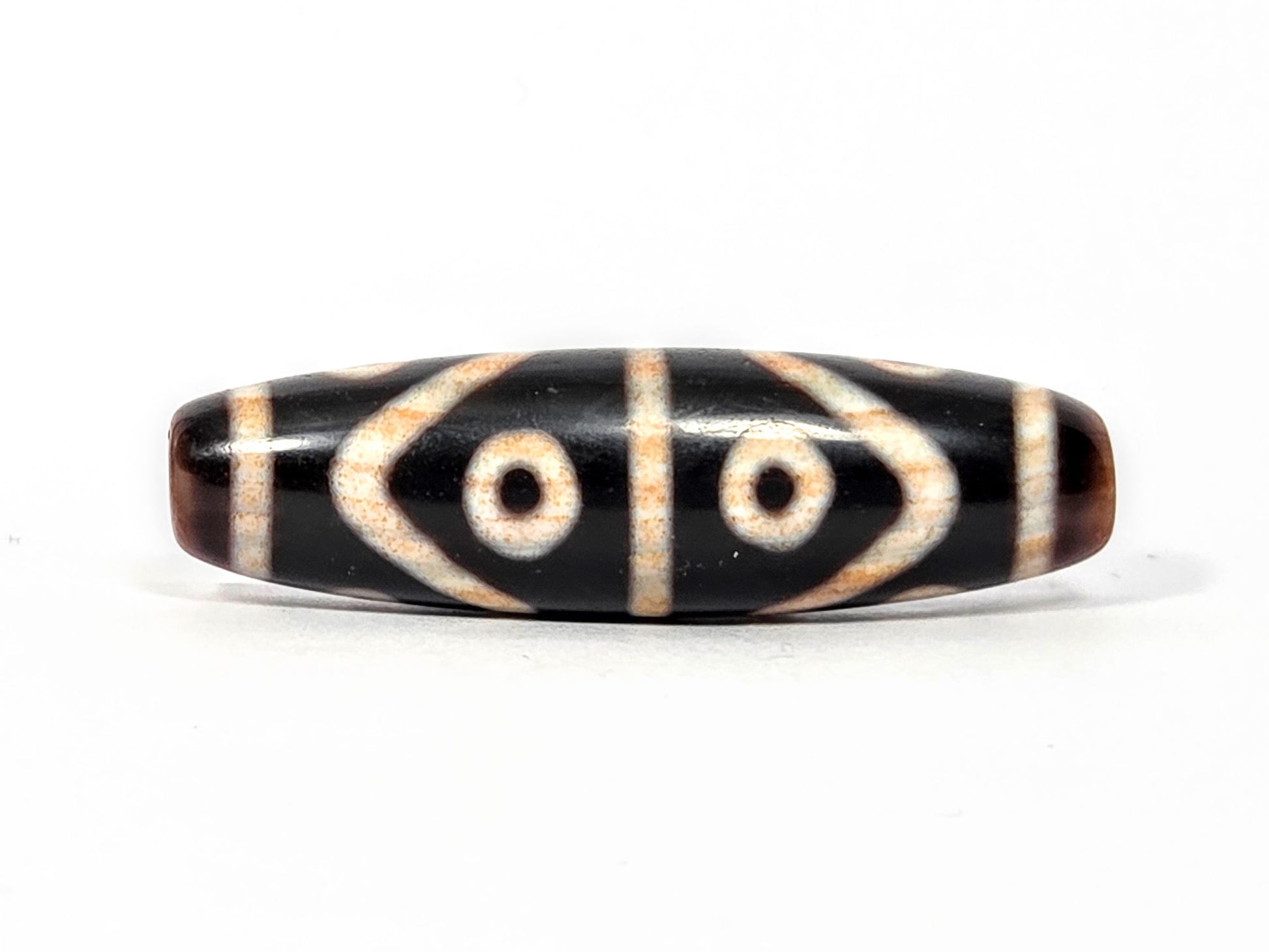 Fourth face of antique Eight Eye Tiger Tooth Dzi — eye circles, tiger tooth forms, warm brown ends