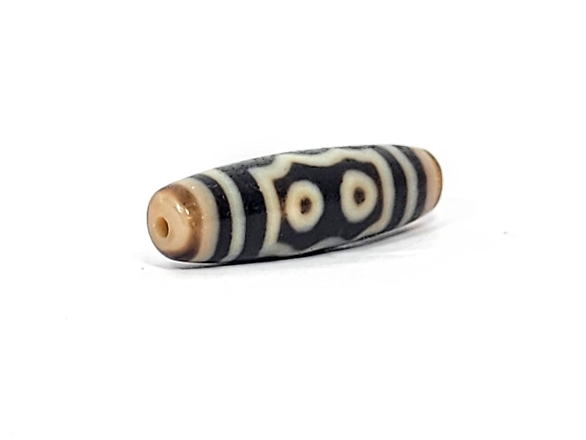 Three-quarter view of antique five eye dzi At-072625-5E, warm honey-tan end cap with drill hole, two-eye frame composition visible, pitch-black torpedo body, unretouched