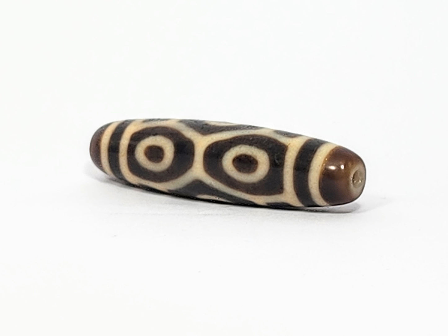 Opposite end of antique Six Eye Naga dzi bead showing drill hole in brown cap and paired cream eye motif, At-050725-6EN3