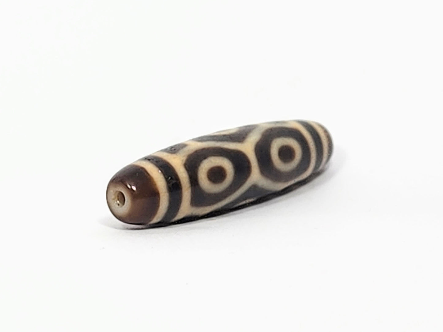 Angled end view of antique Naga dzi bead showing paired Dragon eyes and drill hole in warm brown dome cap, At-050725-6EN3