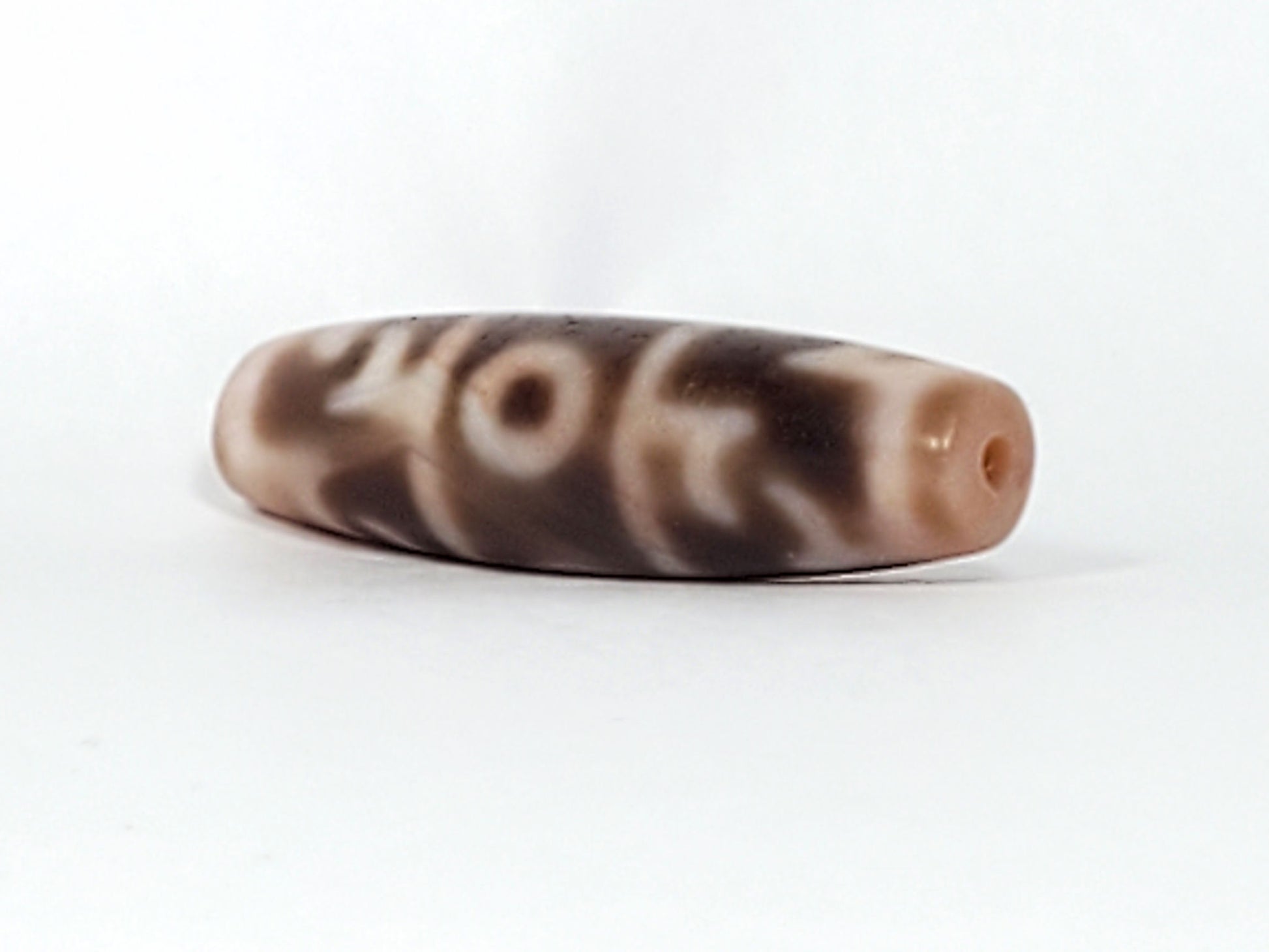 At-060326-GRRP, angled End A, warm cream end cap with drilled hole, paraphernalia motif wrapping body, unretouched