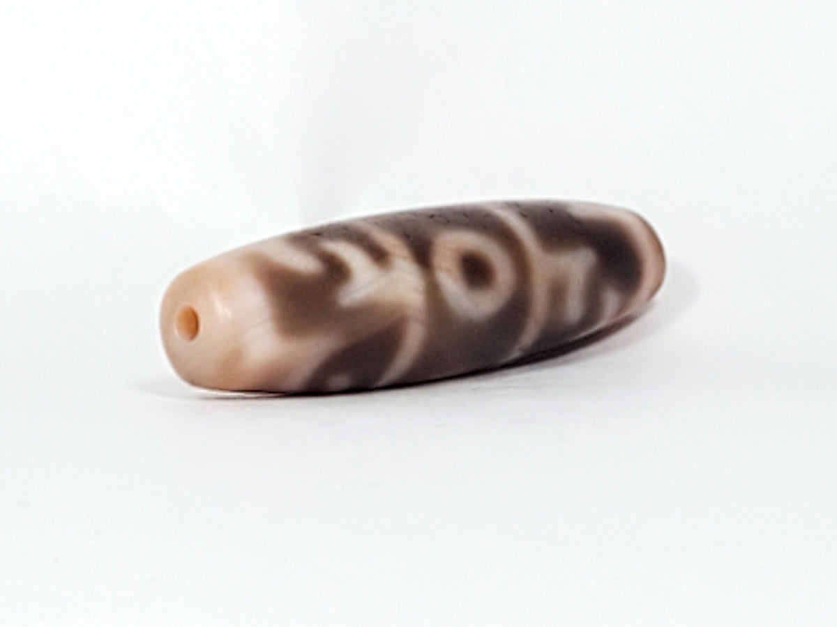 At-060326-GRRP, angled End B, cream end cap and drilled hole, chocolate-brown paraphernalia and eye motif visible, unretouched