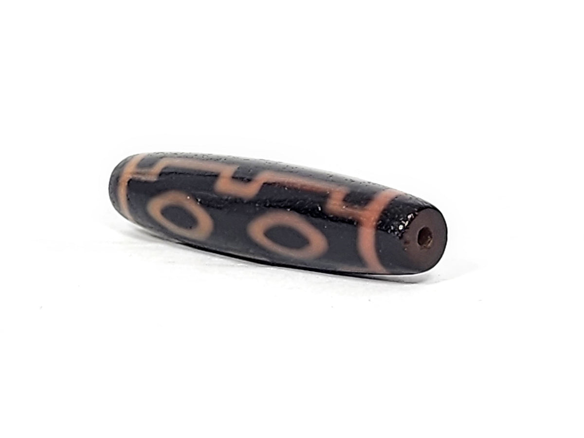 Three-quarter view of antique Four Eye dzi At-012325-4E, dark brown end cap with drill hole, amber motif lines wrapping torpedo body, 51.9mm × 12.2mm, unretouched