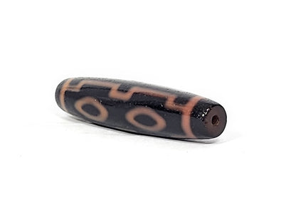 Three-quarter view of antique Four Eye dzi At-012325-4E, dark brown end cap with drill hole, amber motif lines wrapping torpedo body, 51.9mm × 12.2mm, unretouched
