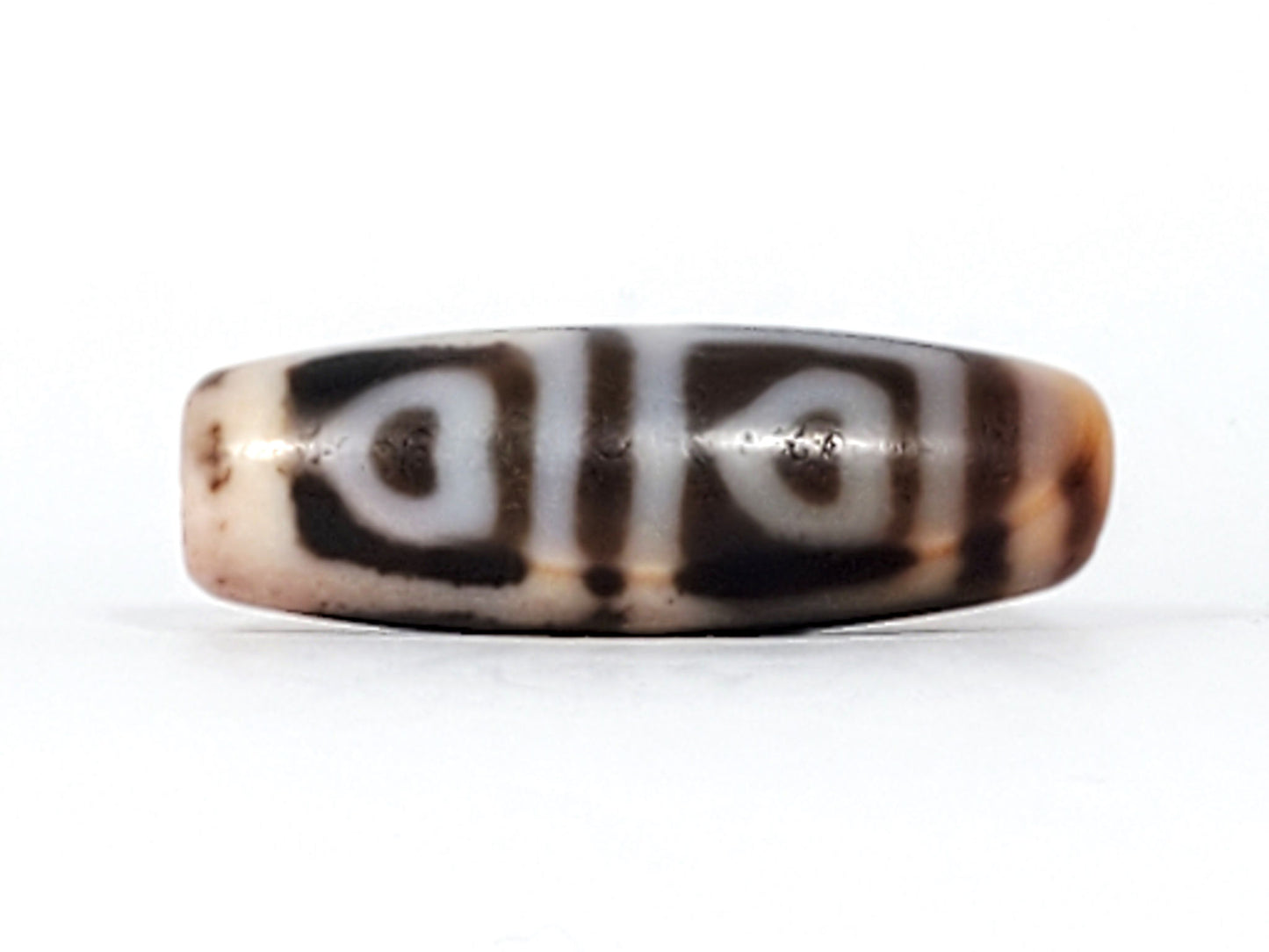 Angled view of antique Four Leaf Bodhi dzi At-101624-FLB, amber agate barrel form, cream four-leaf motif, cinnabar bloodspot inclusions visible on surface, 35.7mm