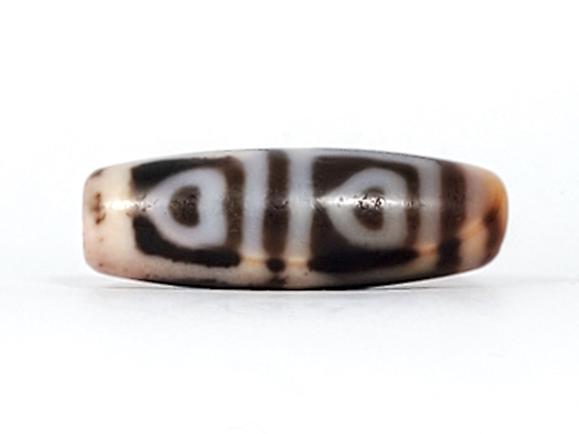 Angled view of antique Four Leaf Bodhi dzi At-101624-FLB, amber agate barrel form, cream four-leaf motif, cinnabar bloodspot inclusions visible on surface, 35.7mm