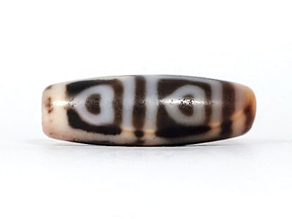Angled view of antique Four Leaf Bodhi dzi At-101624-FLB, amber agate barrel form, cream four-leaf motif, cinnabar bloodspot inclusions visible on surface, 35.7mm
