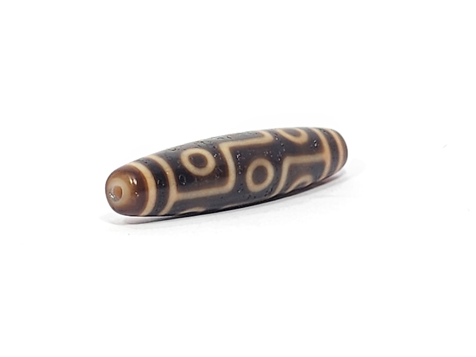 Angled end view of antique Nine Eye dzi bead showing warm amber-brown rounded end cap and drill hole, At-051525-9E2