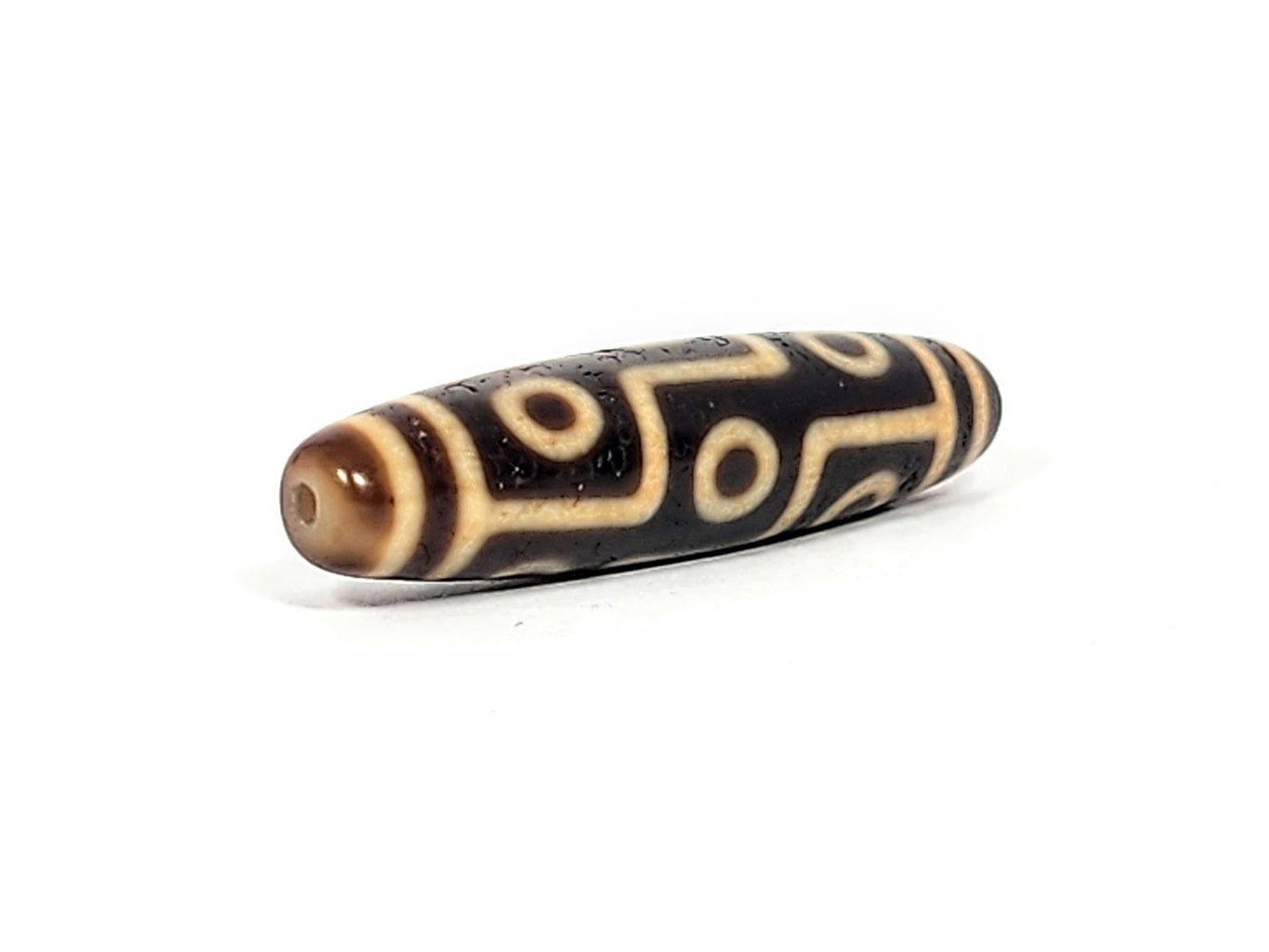 Angled end view of antique Nine Eye dzi bead showing drill hole in warm brown cap and eye network on body, At-011625-9E