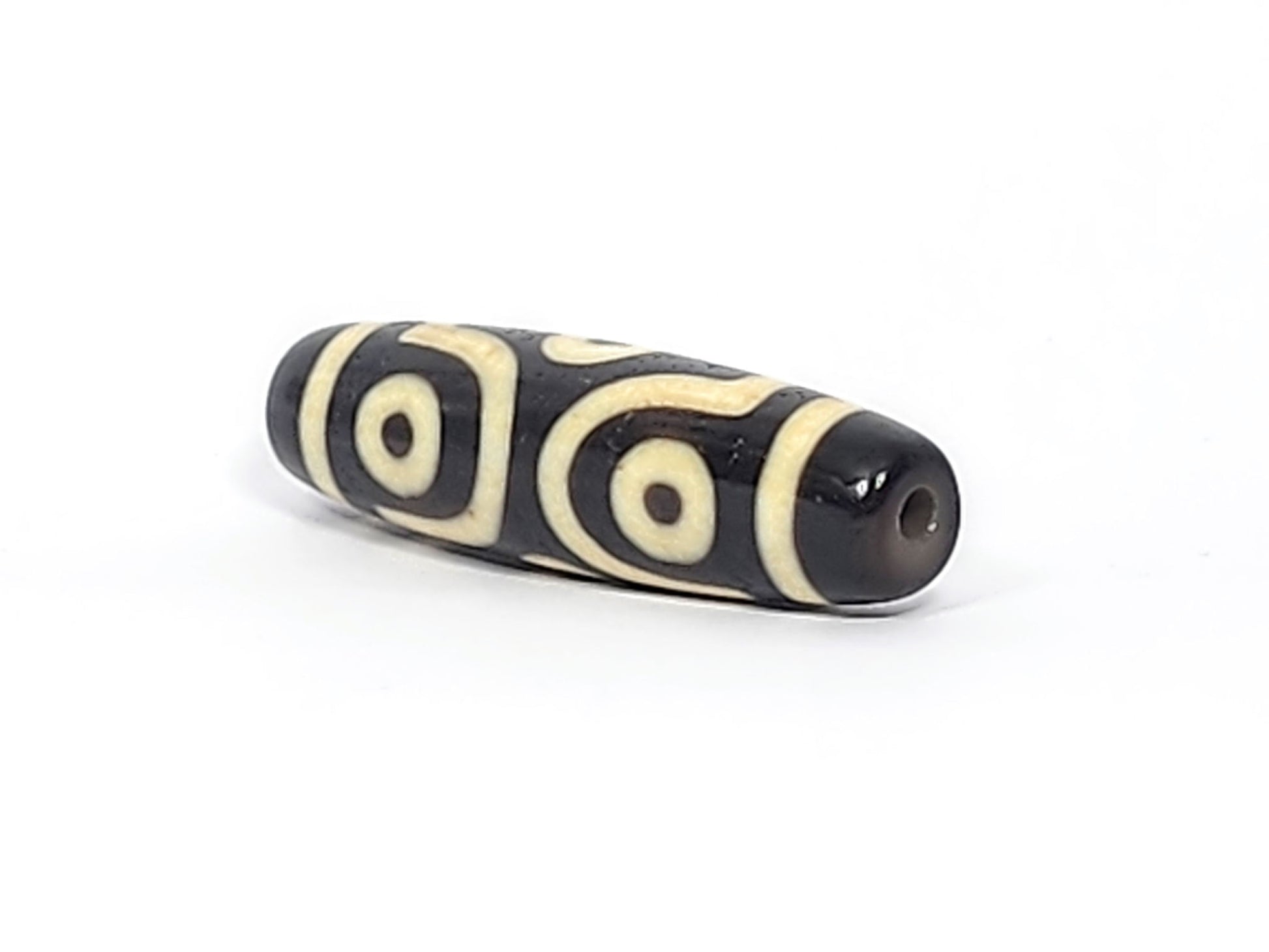 Three-quarter view of antique six eye dzi At-042925-6E2, pitch-black end cap with drill hole, two C-ring eyes and scroll visible, elongated torpedo body, unretouched