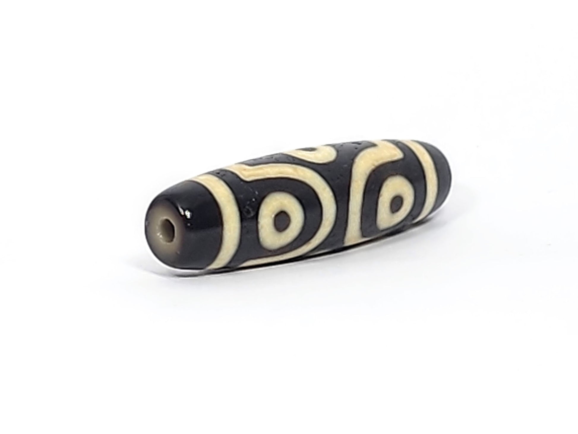 Opposite end cap of antique six eye dzi At-042925-6E2, pitch-black agate tip, drill hole, C-ring eyes and scroll motif visible on body, 41.4mm × 11.4mm, unretouched photography