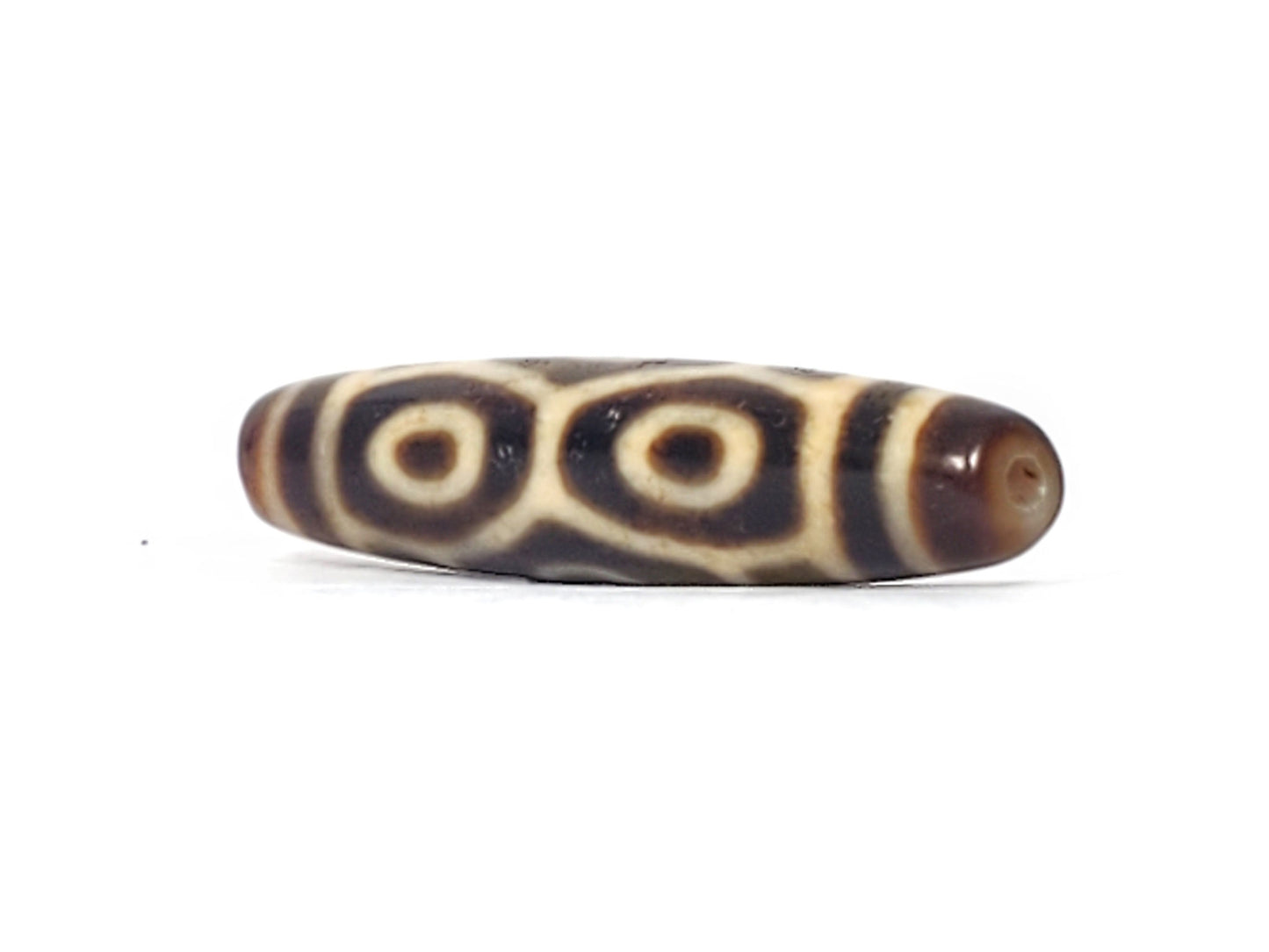 Angled end view of antique Naga Dragon Eye dzi bead showing paired eyes and drill hole in dark brown cap, At-092524-6EN