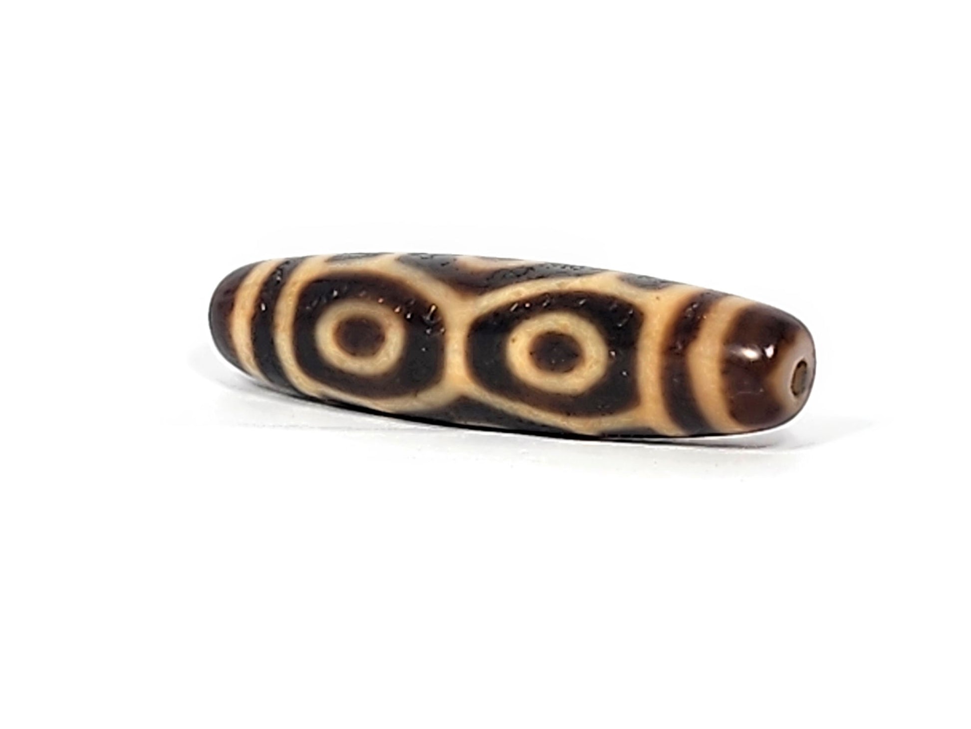Angled end view of antique Naga dzi bead showing two paired Dragon eyes and drill hole in warm brown cap, At-122124-6EN2