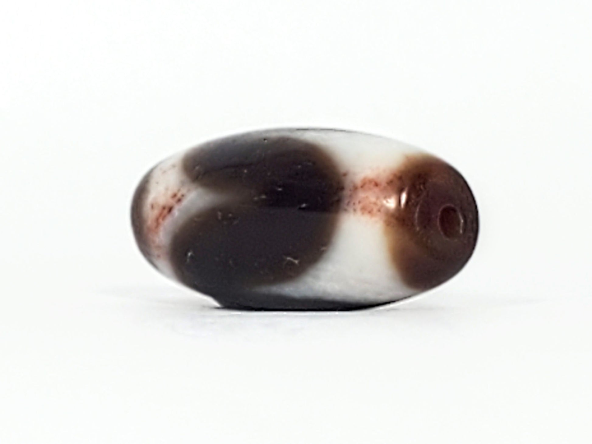 End cap of antique Tasso dzi At-093024-TaBS3, deep brown agate tip with centred drill hole, wide barrel body, cream Tasso zones with bloodspot inclusions visible, unretouched